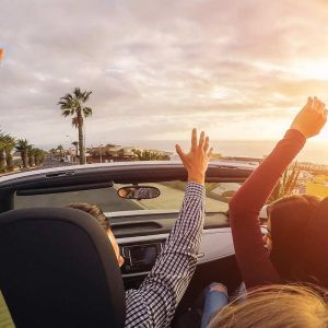 friends riding a convertible car with their hands up while doing a road trip from Toronto