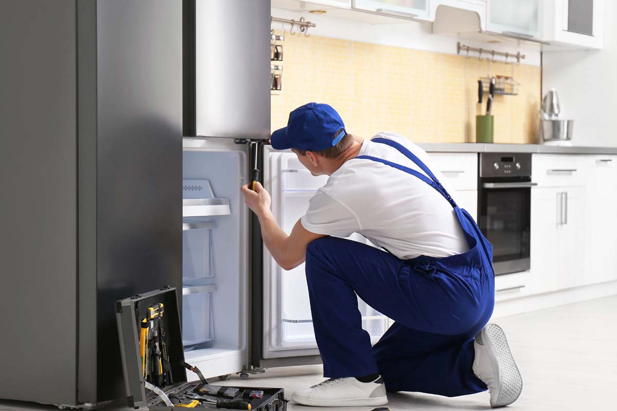 Technician repairing refrigerator in kitchen