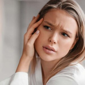 Acne-wrinkles prone skin concept. Sad lady looking at mirror and checking her face skin